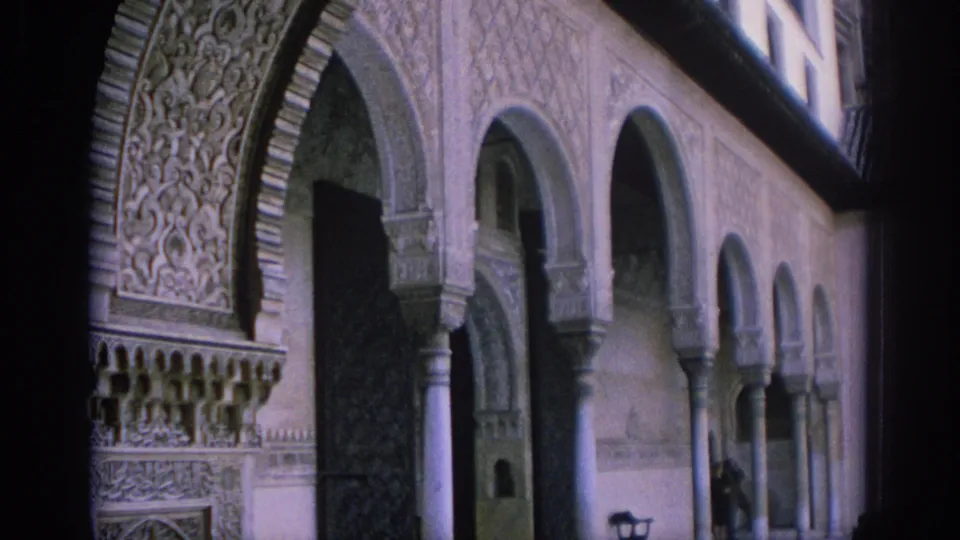 1966 Spain 8mm frame showing a Moorish-style courtyard arcade with a distant visitor near the columns.