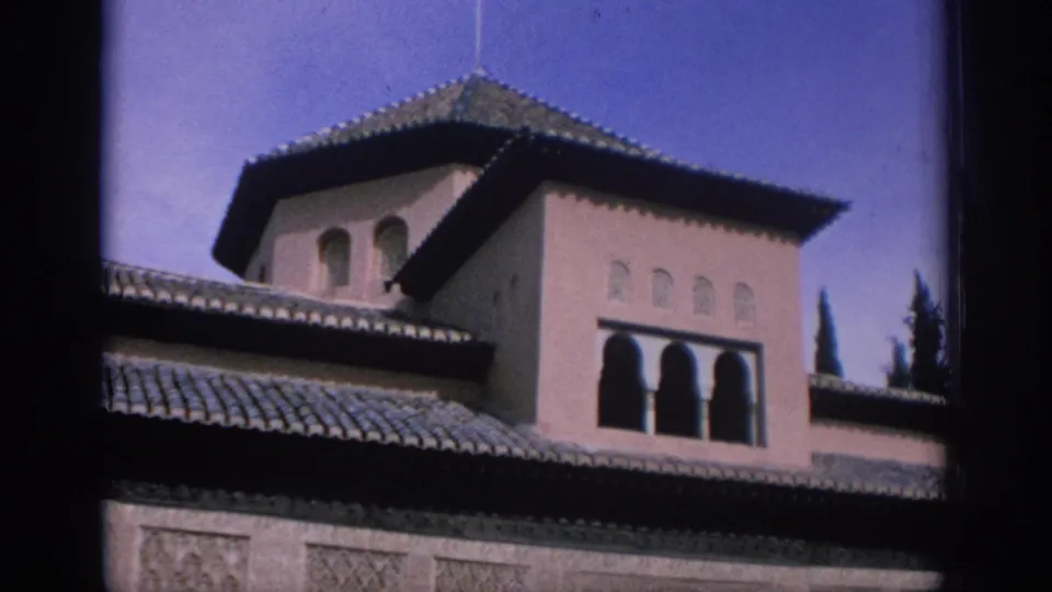 1966 Spain 8mm frame showing an exterior roofline with arched windows, tiled roofs, and clear sky.
