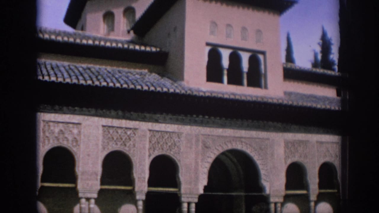 Arched colonnade beneath a tiled roof with tower windows and trees behind.