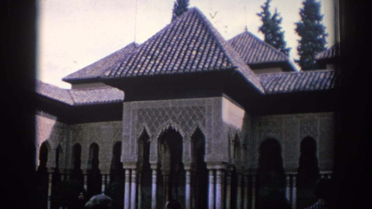 1966 Spain 8mm frame showing a Moorish-style courtyard arcade with tiled roofs, carved arch panels, columns, and visitors partly silhouetted below.
