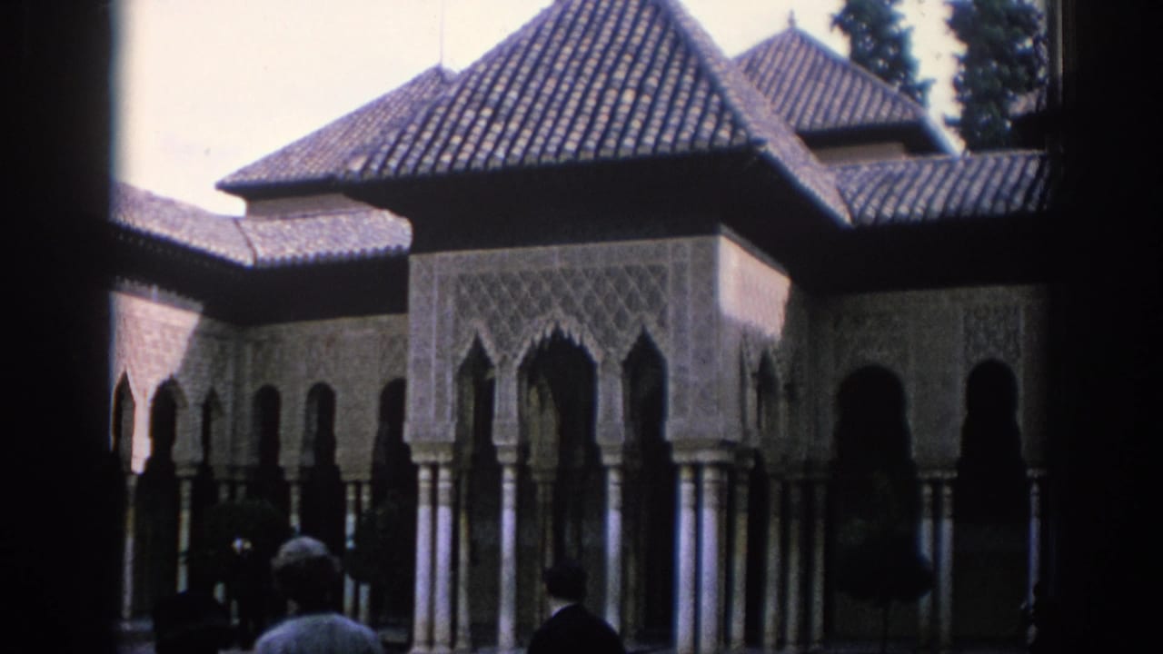 1966 Spain travel footage frame with tiled roofs, decorated archways, columned arcades, and visitors observing the courtyard architecture.
