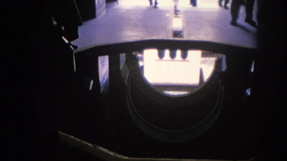 1966 Spain home-movie frame with a dark grille-like foreground and a bright architectural view beyond, including partial visitors at the edge.