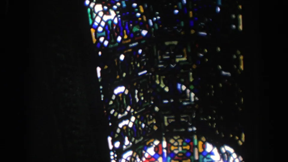 Visitor-shot 1966 Spain frame with a vertical stained glass section, strong contrast, and soft 8mm grain inside a historic building.