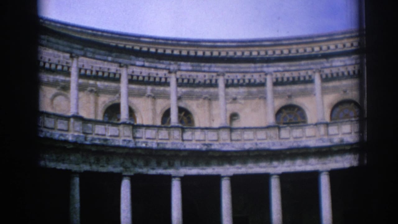 1966 Spain 8mm frame showing a low-angle view of a curved stone building with columns, balcony rail, arched windows, and blue sky.