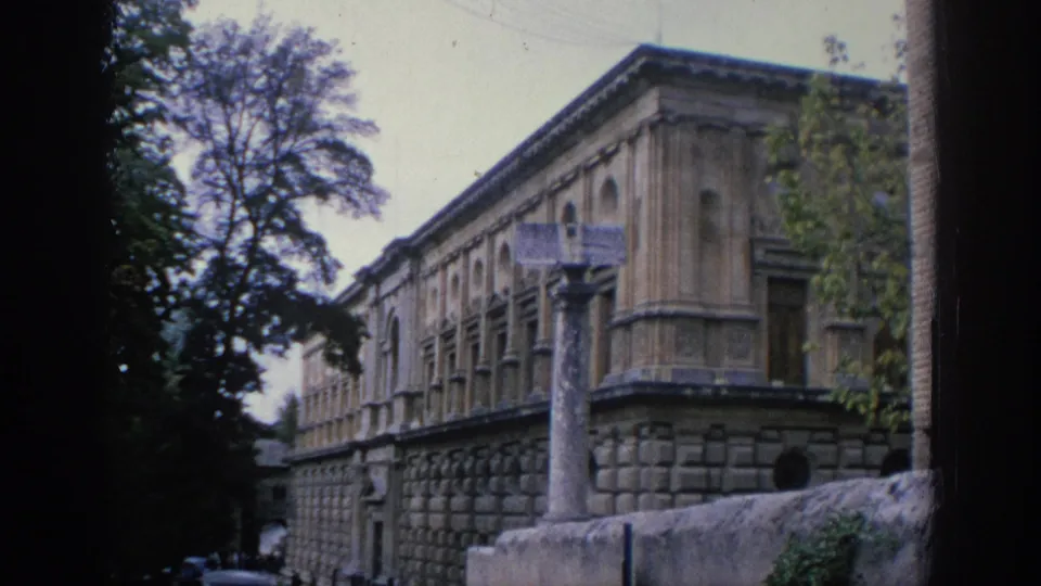 1966 Spain 8mm frame with a side view of an ornate stone facade, tree silhouettes, a freestanding column, and a low stone wall.