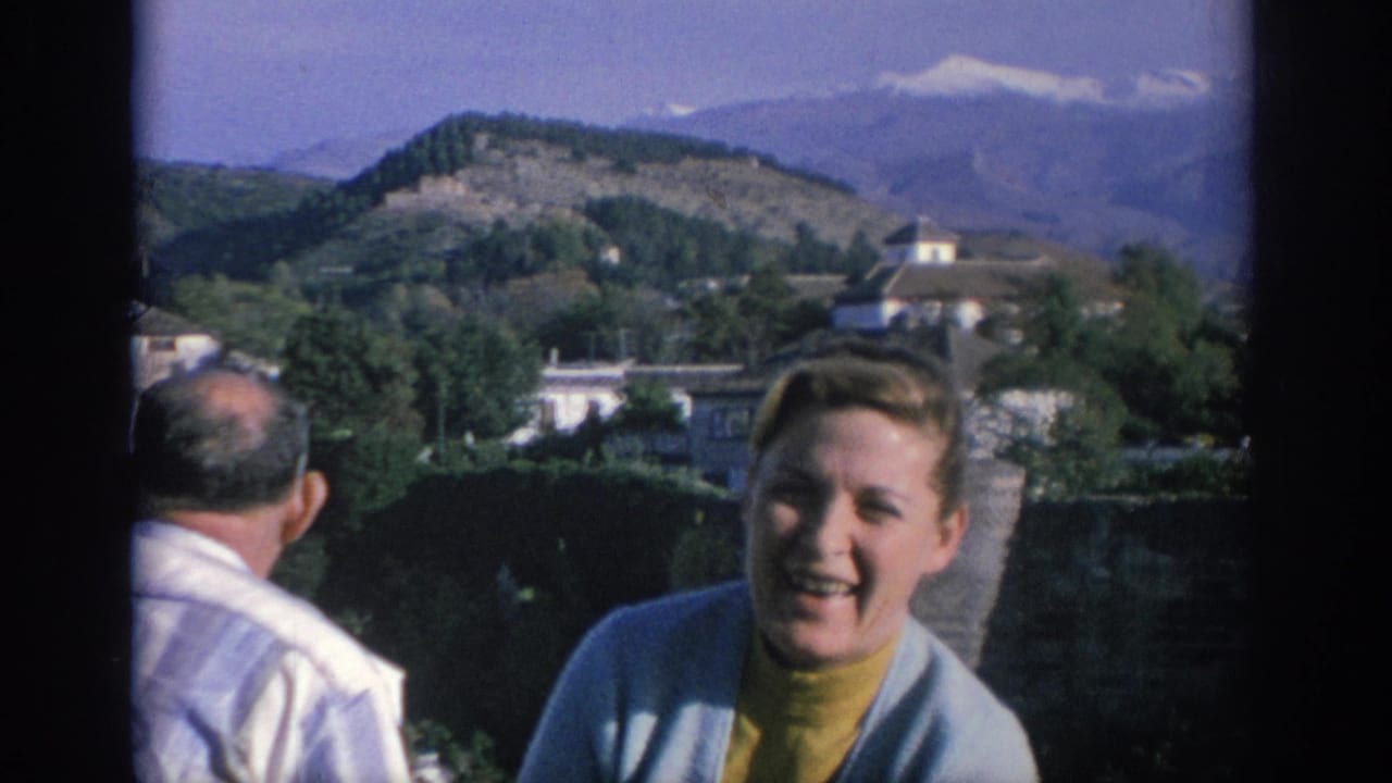 Woman smiling near a stone wall with a man turned away and mountains behind them.