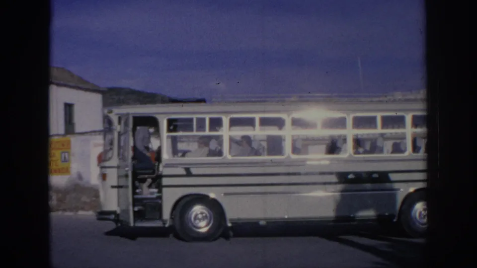 1966 Spain frame of a white bus with passengers visible through the windows, captured with dark contact-sheet borders and soft 8mm color.
