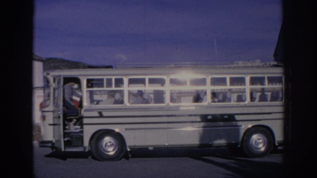 1966 Spain 8mm frame showing a white striped bus stopped in bright sun, with several passengers seen through the windows.