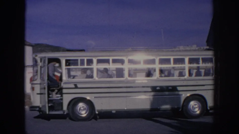 1966 Spain 8mm frame showing a white striped bus stopped in bright sun, with several passengers seen through the windows.