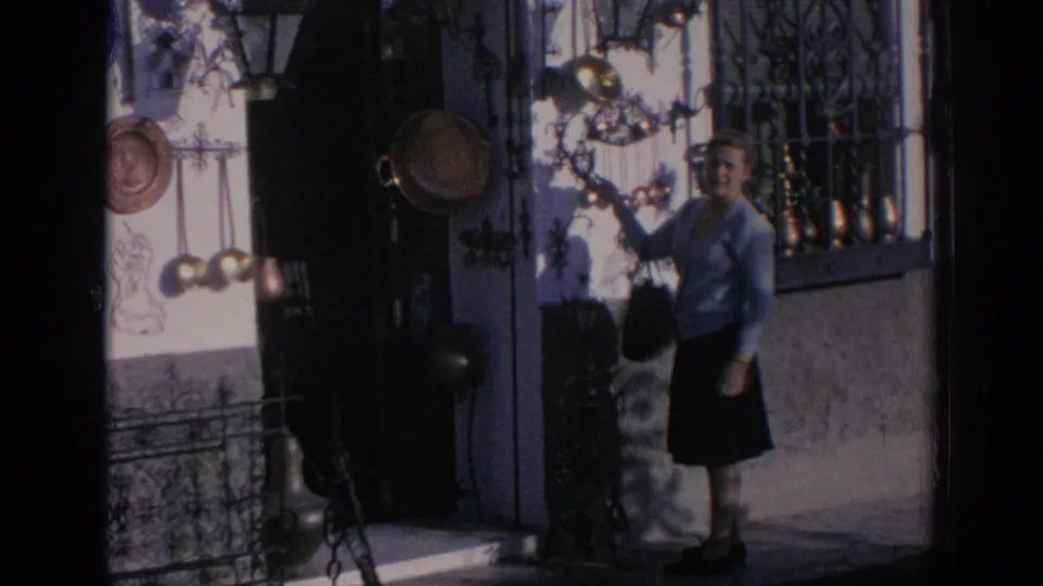 1966 Spain 8mm frame showing a woman browsing brass and copper cookware displayed outside a small street shop.
