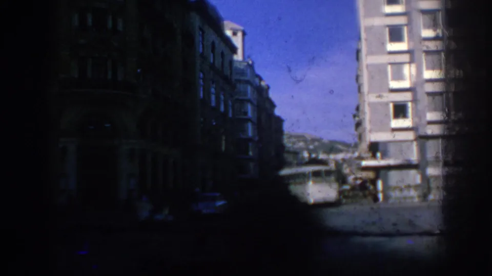 Underexposed 1966 Spain street view with a white bus, apartment facade, older buildings, and heavy dark film borders.