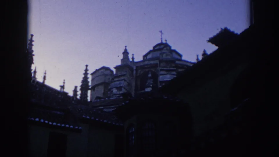 1966 Spain 8mm frame showing dark foreground edges around old rooflines and an ornate building facade, with cool color shift and soft focus.