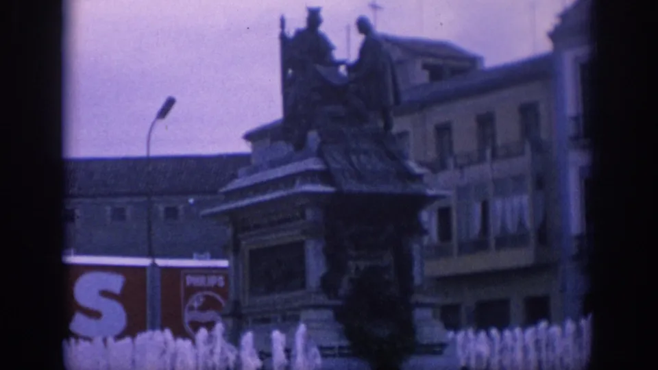 1966 Spain 8mm frame showing fountain water jets, a statue monument, older city buildings, and a partial Philips advertisement in the background.