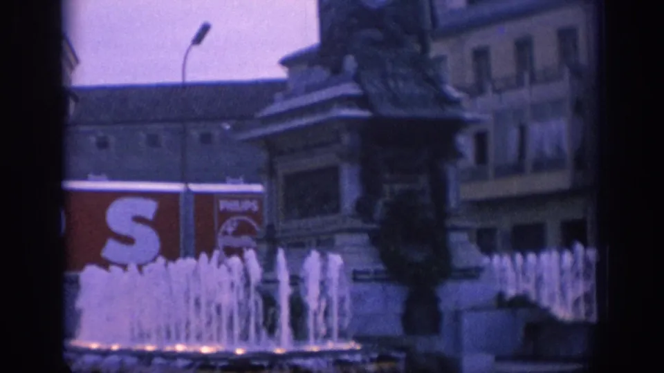 1966 Spain city-square frame with bright fountain jets, a large statue monument, older building facades, and a visible Philips advertisement.