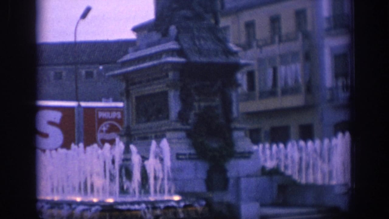 1966 Spain 8mm frame showing a public fountain, statue monument, balconies, and a visible Philips sign in the background.