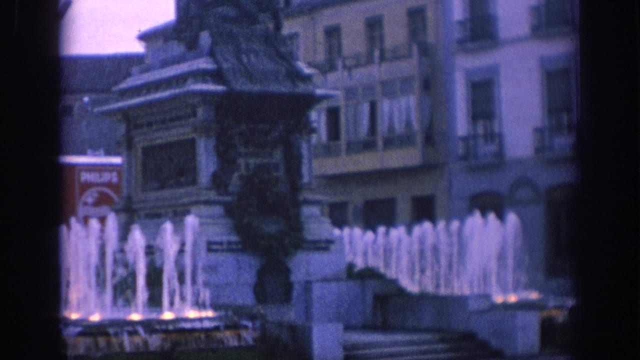 Statue fountain with water jets and buildings behind it.