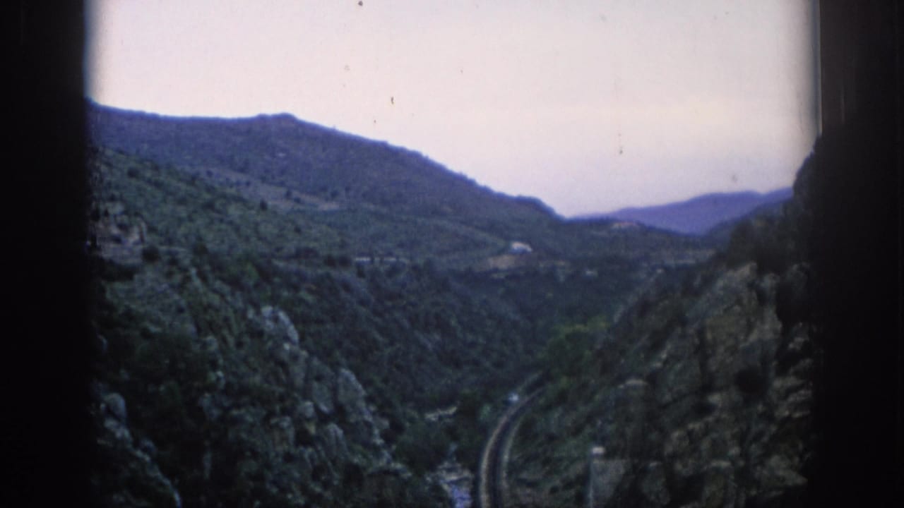 1966 Spain 8mm travel frame showing a green mountain valley, rocky slopes, distant hills, and a railway track below.