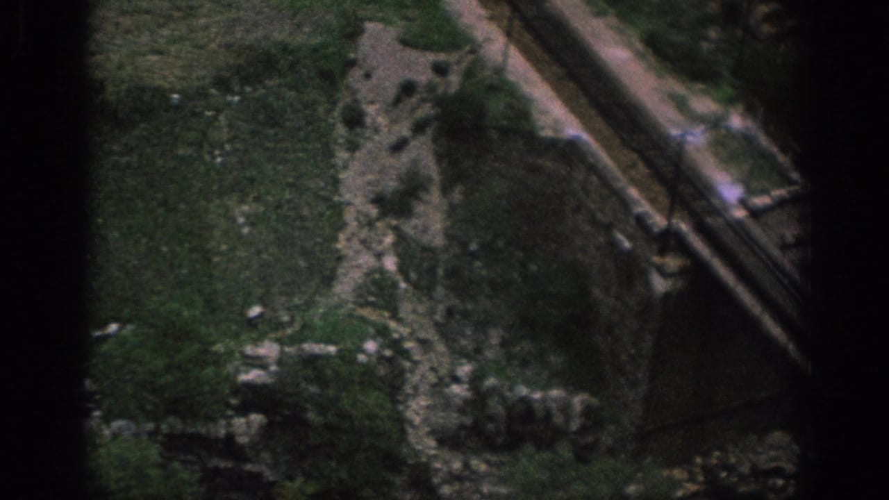 Dirt path and end of a stone bridge crossing rough green terrain.