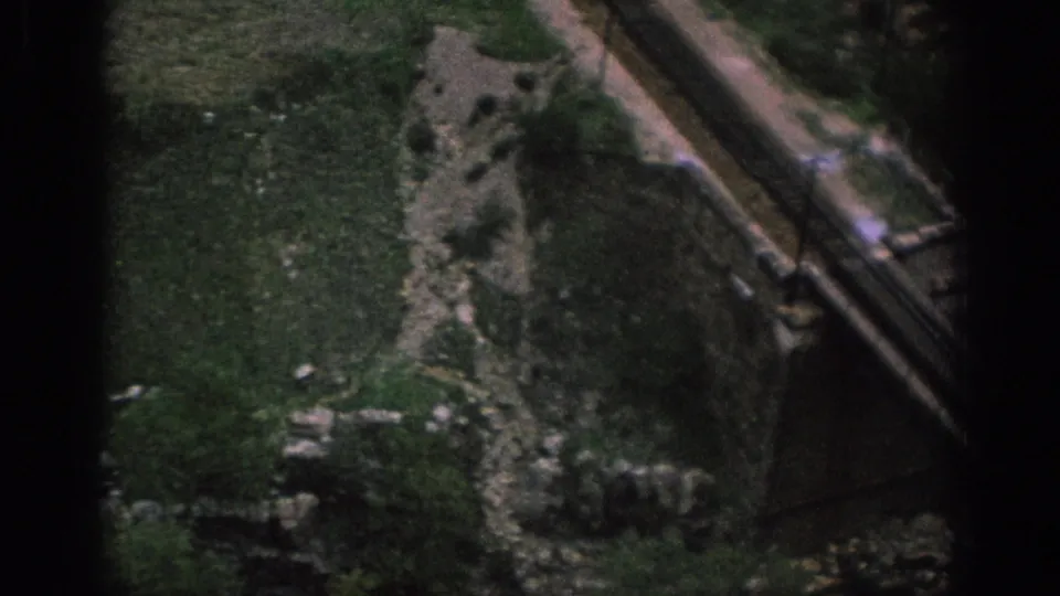 1966 Spain 8mm frame showing the approach to a weathered stone bridge beside a narrow dirt path and scrubby ground.