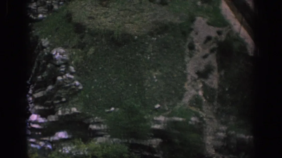 1966 Spain 8mm frame surveying grassy ground, scattered rocks, and a narrow path near the bridge area.