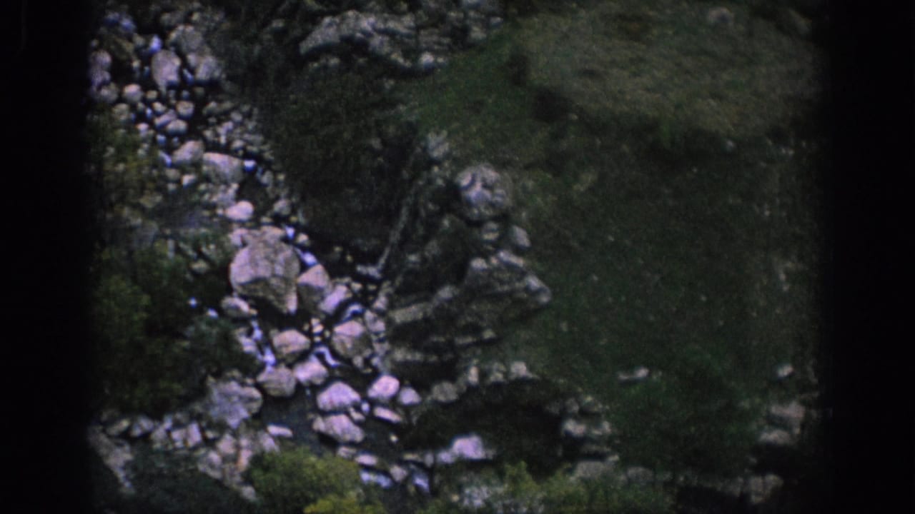 Spain 1966 home-movie frame showing a rocky stream bed and shadowed mountain vegetation within visible film borders.