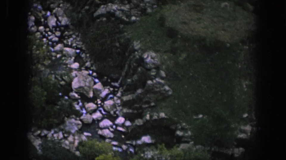 Spain 1966 home-movie frame showing a rocky stream bed and shadowed mountain vegetation within visible film borders.