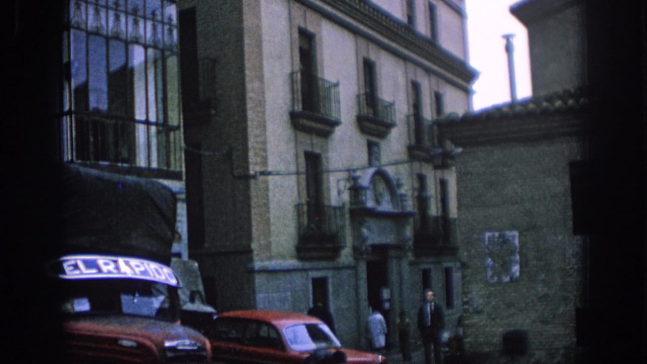 Street view with old buildings, a red sedan, a dark delivery vehicle, and several pedestrians.