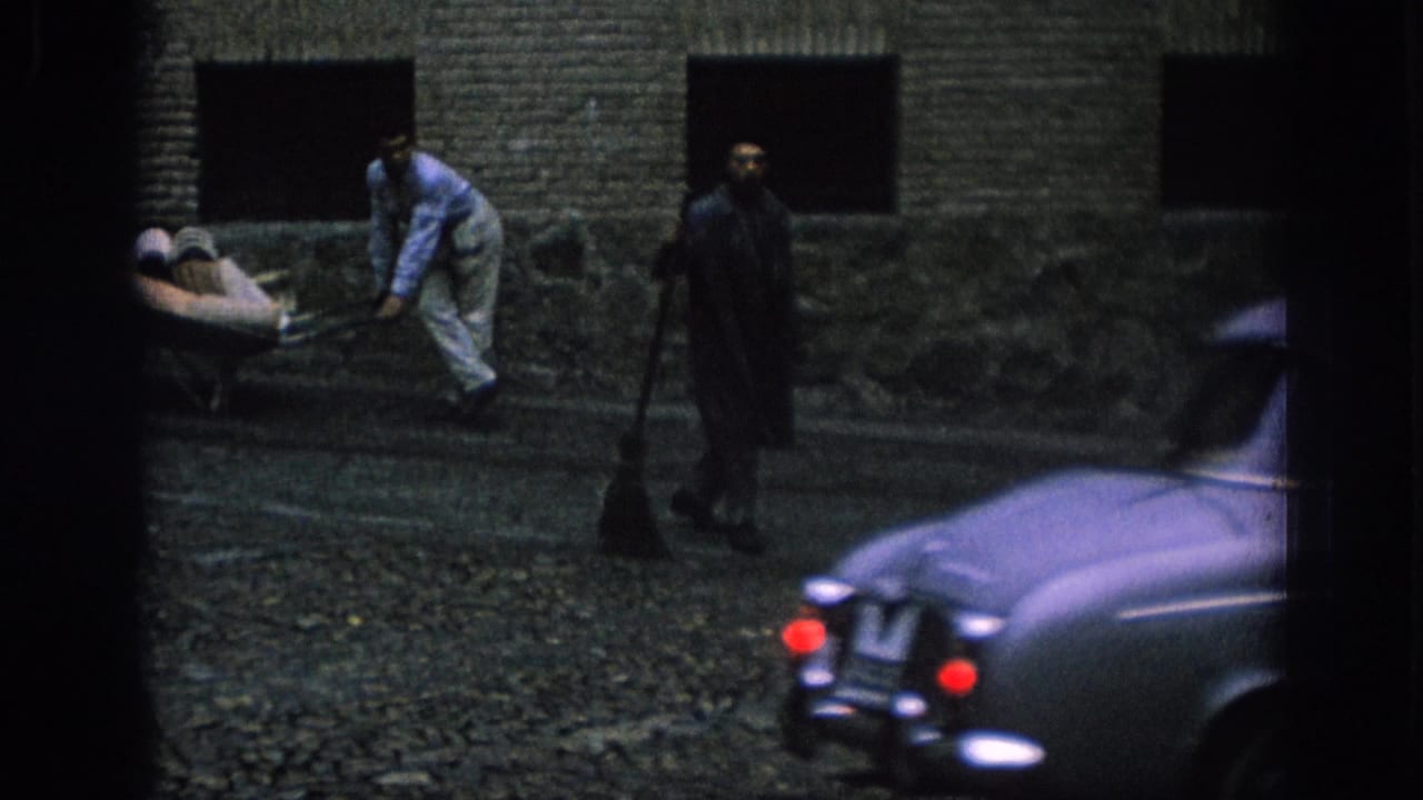 In Spain, 1966, two men appear to clean a cobblestone street beside a wall while a rounded mid-century car sits partly in frame.