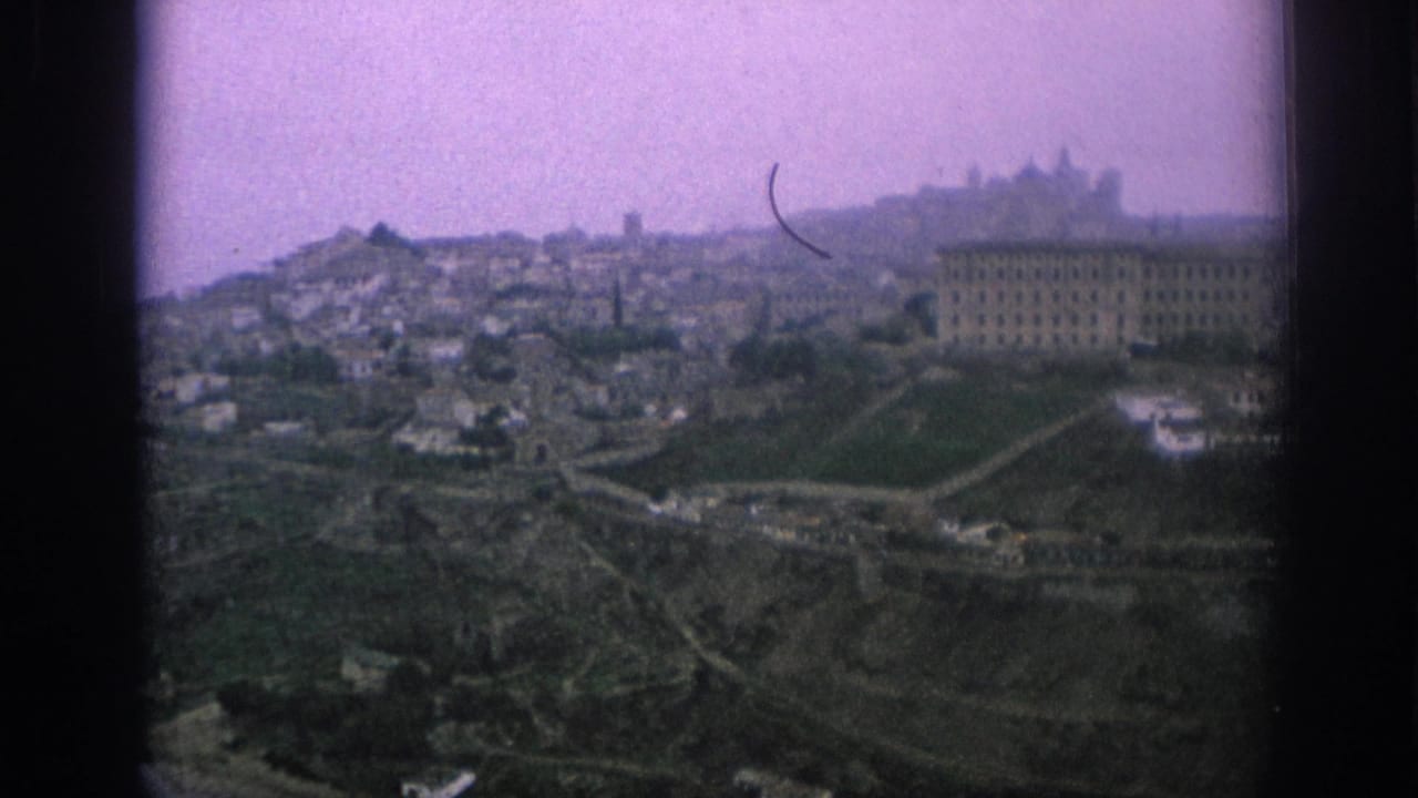 1966 Spain 8mm frame showing a hazy elevated panorama of a hillside city with terraced slopes and a prominent institutional-looking building.