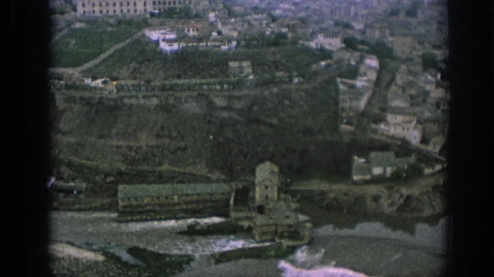 1966 Spain frame showing a sloped city edge with terraces, scattered buildings, a riverside or waterway area, and dark 8mm frame borders.