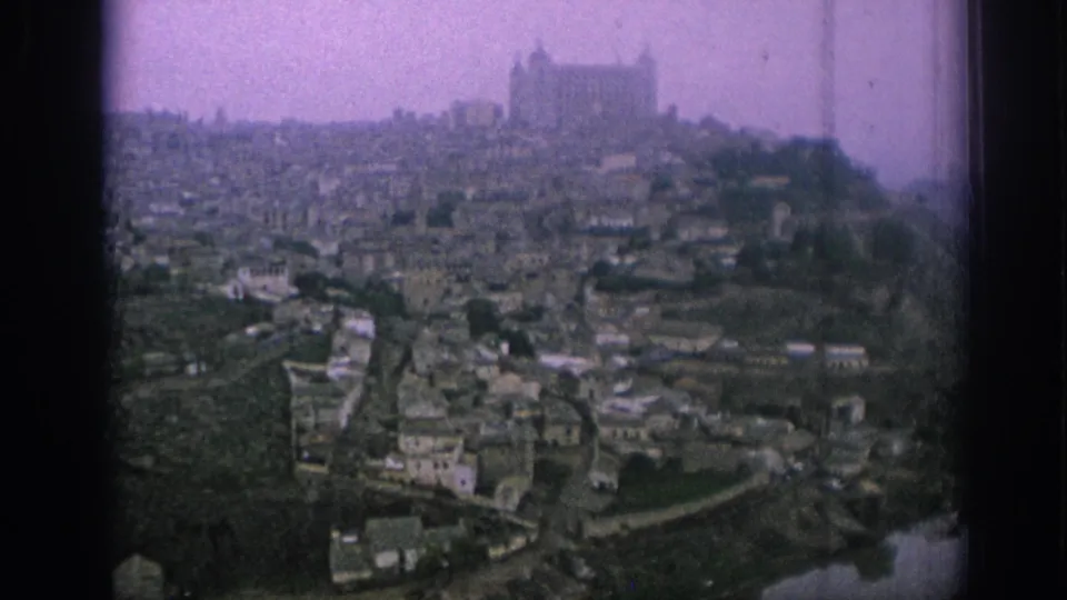 1966 Spain 8mm frame with a wide elevated view over the settlement, river edge, terraced slopes, and distant hilltop landmark.