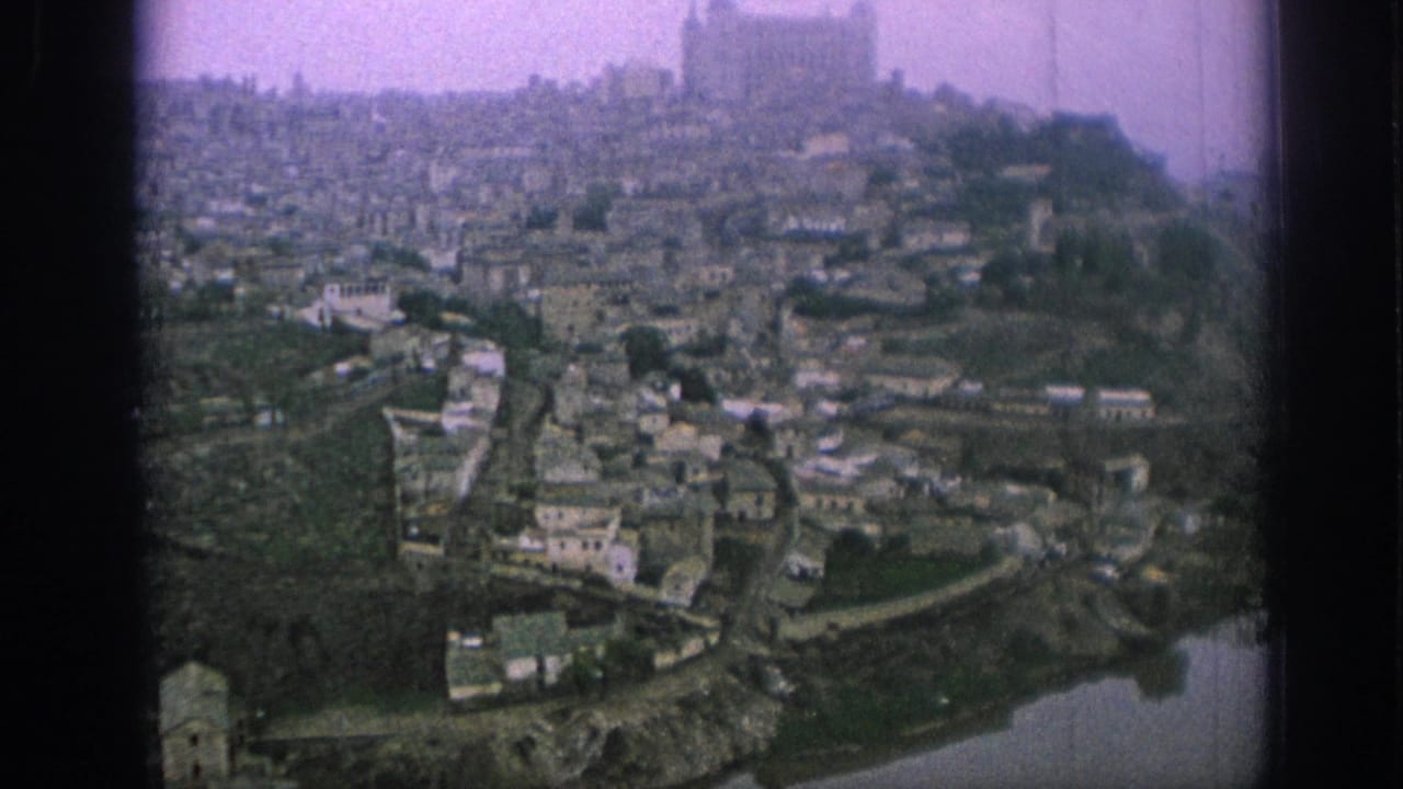 1966 Spain home-movie frame showing a historic riverside hill town with clustered buildings and a prominent church above the valley.