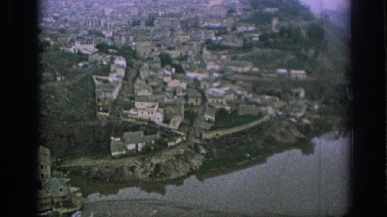 1966 Spain frame looking over a historic town beside a river, with pale buildings and sloped terrain filling the view.