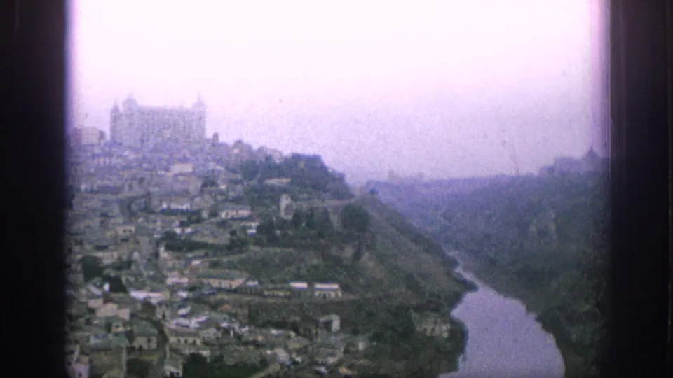 Overexposed 1966 Spain home-movie view of a hilltop church and town descending toward a narrow river valley.