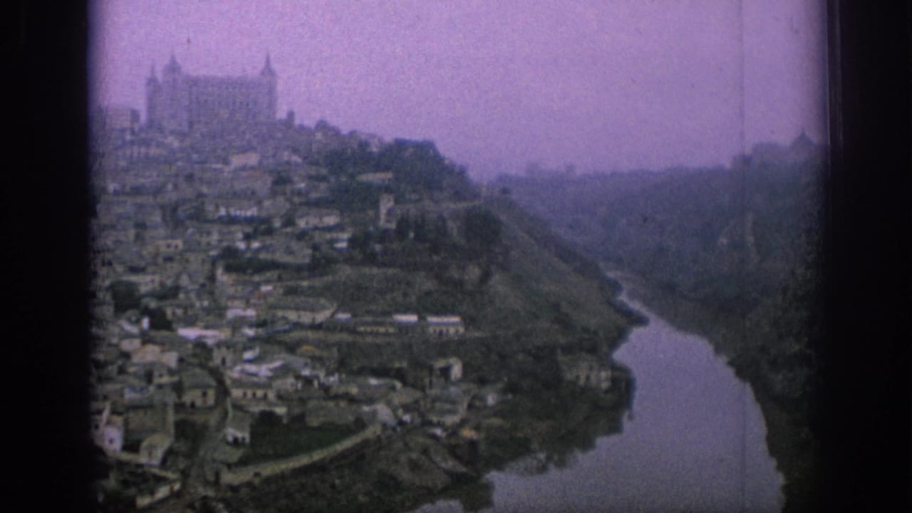 1966 Spain 8mm view of a hillside town above a river, with a castle-like structure on the summit and soft purple film cast.