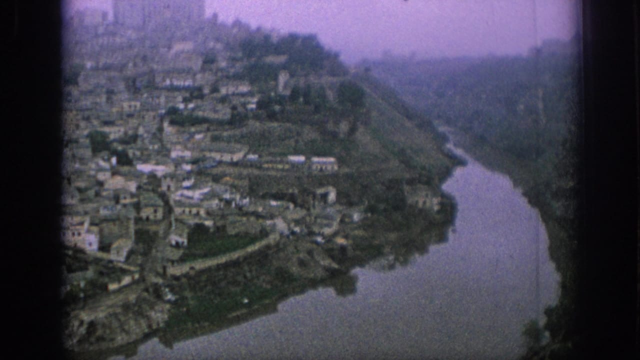 Closer view of hillside buildings descending toward a river bend below a hazy ridge.