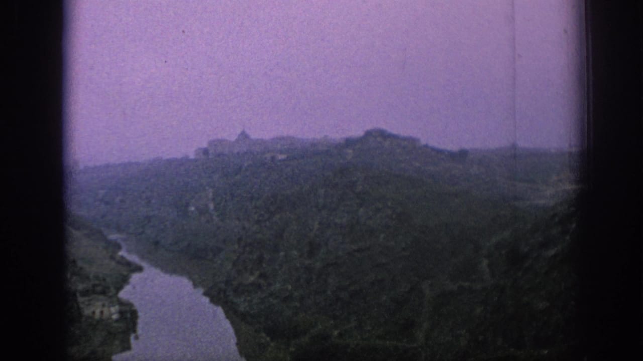 1966 Spain 8mm frame showing a winding river through hills with distant masonry buildings and a purple color cast.