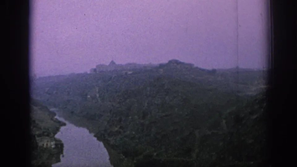 1966 Spain 8mm frame showing a winding river through hills with distant masonry buildings and a purple color cast.