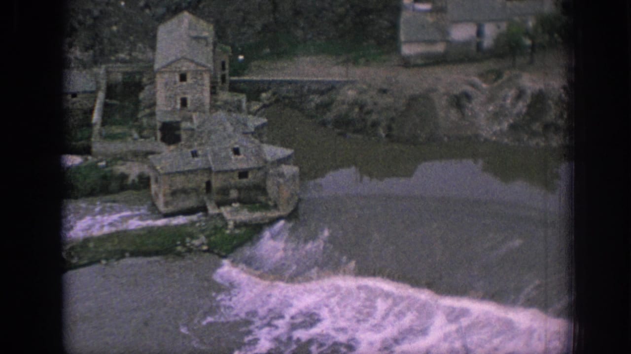 Stone riverside building beside a low dam with white water spilling across the river.