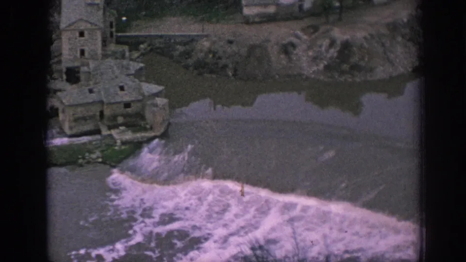 1966 Spain 8mm frame showing the edge of a stone mill-like structure and white water below a riverside weir.