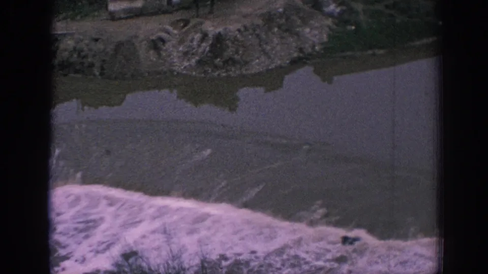 1966 Spain 8mm frame focused on the river below the waterworks, with foam, bank terrain, and dark film edges visible.