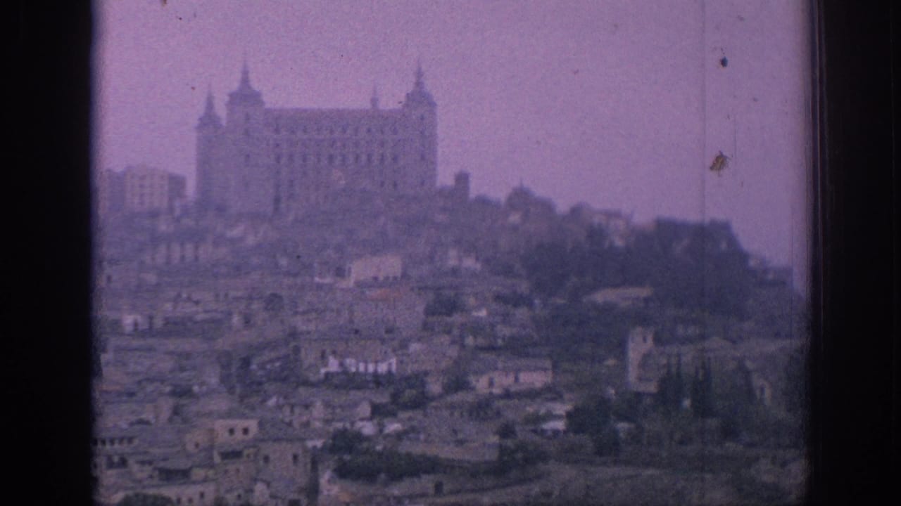 1966 Spain home-movie view of a large hilltop landmark above clustered rooftops and trees, with soft grain and purple color cast.