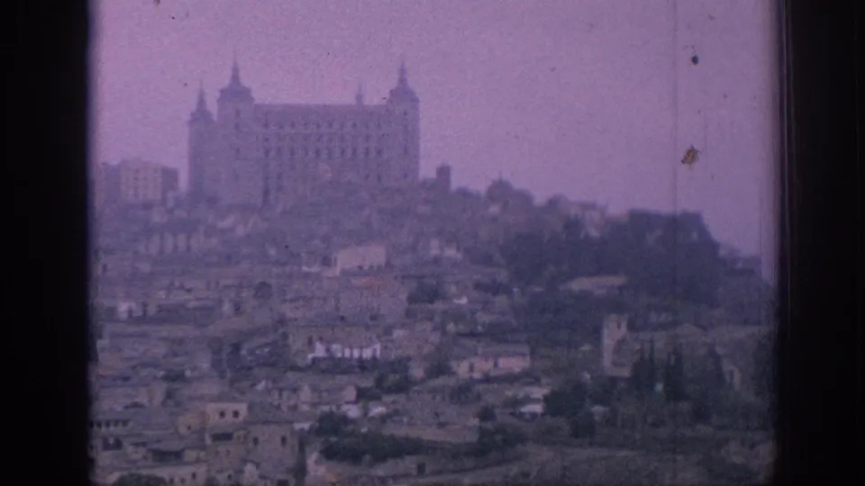 1966 Spain home-movie view of a large hilltop landmark above clustered rooftops and trees, with soft grain and purple color cast.