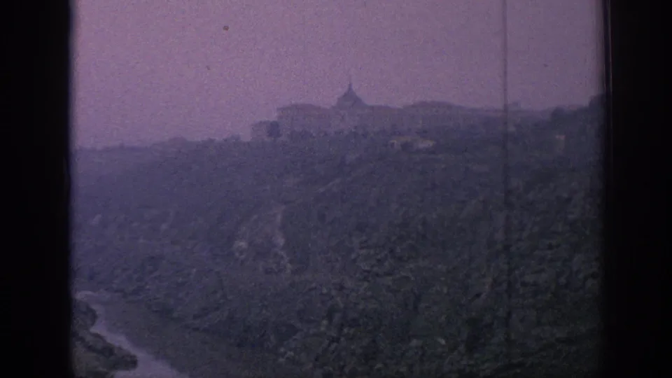 A 1966 Spain landscape view shows a ridge-top structure, steep vegetated hillside, and valley edge, rendered in grainy aged 8mm color.