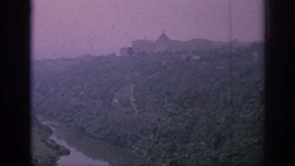 1966 Spain home-movie view of a mountain village or ridge-top town above a winding river valley, with faded color and soft focus.
