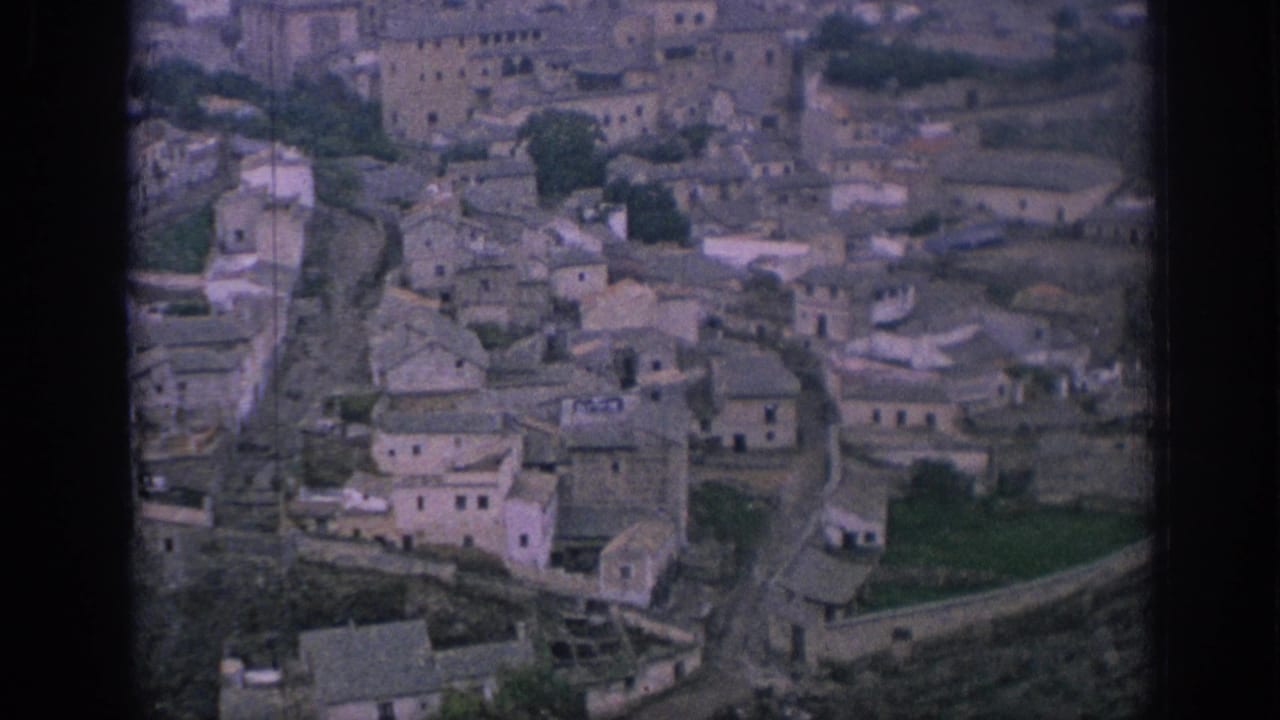 High-angle 1966 Spain view over clustered stone buildings, narrow roads, and terraced slopes in a mountain village.