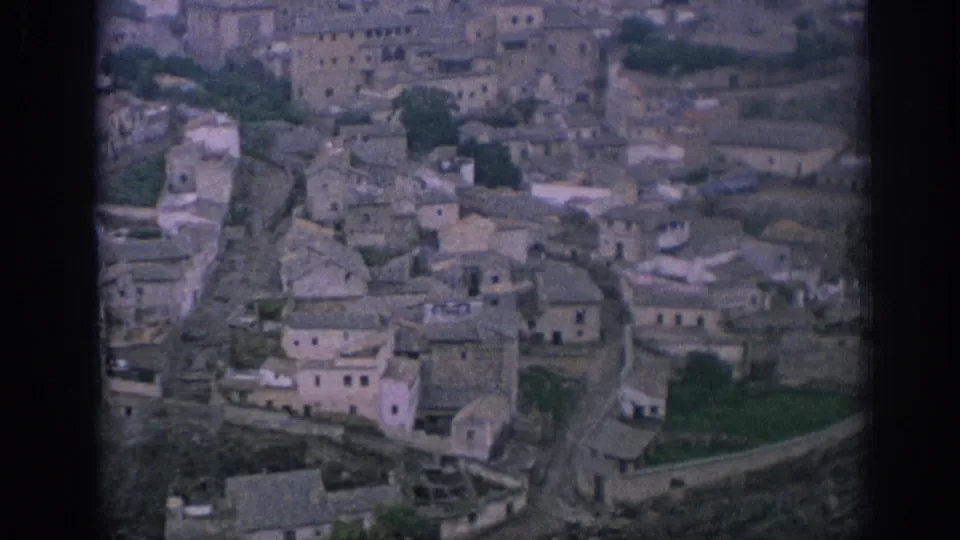 Elevated home-movie view of a Spanish mountain village with stone houses, narrow lanes, and stepped terrain.