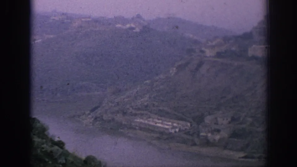 Hazy 1966 Spain home-movie view across a river bend and steep mountain slopes above the village area.
