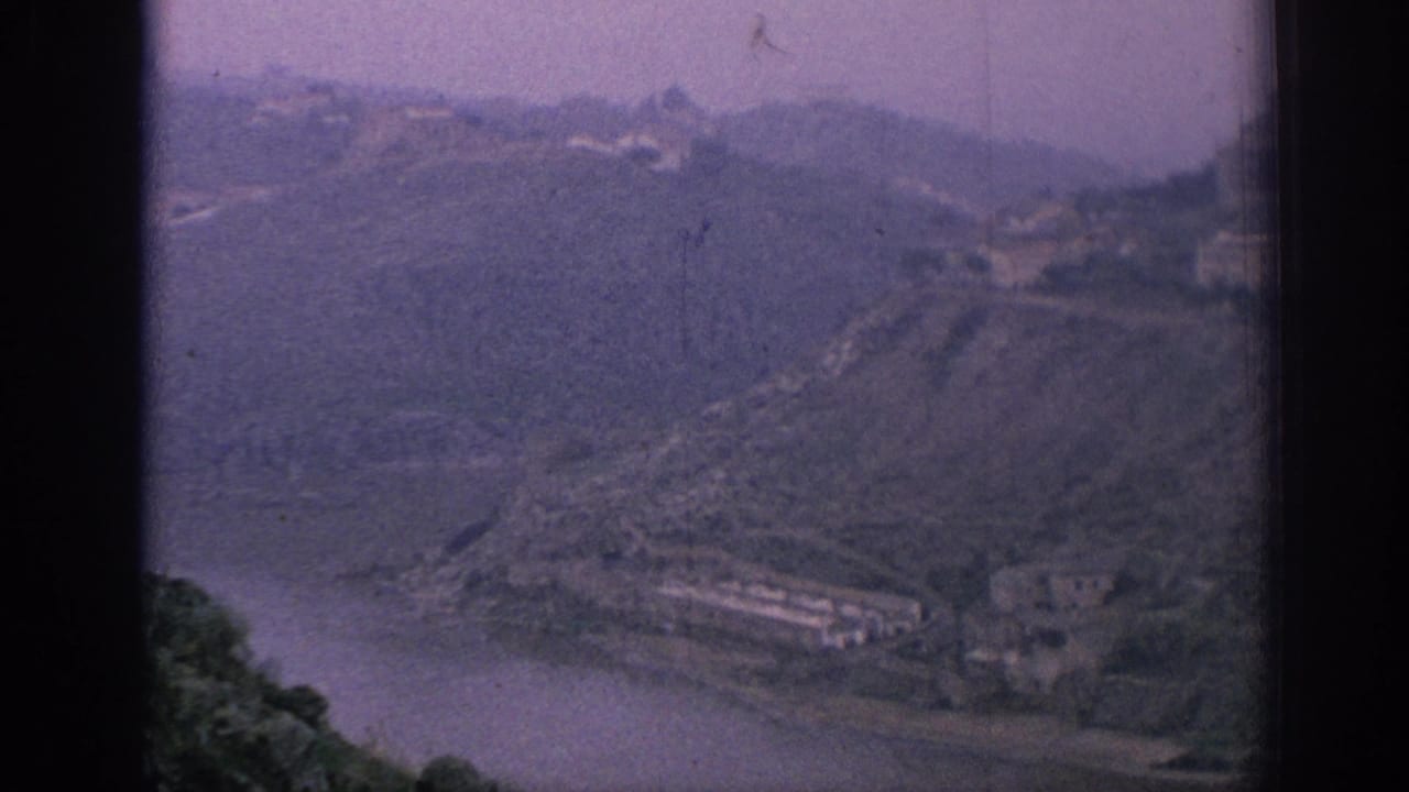 High view of a river bend beside steep hills and scattered buildings.