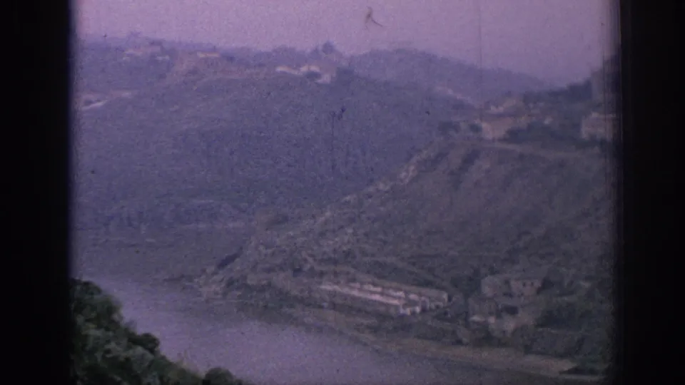 1966 Spain 8mm frame showing a high view over a river bend, wooded slopes, and a few buildings along the hillside.